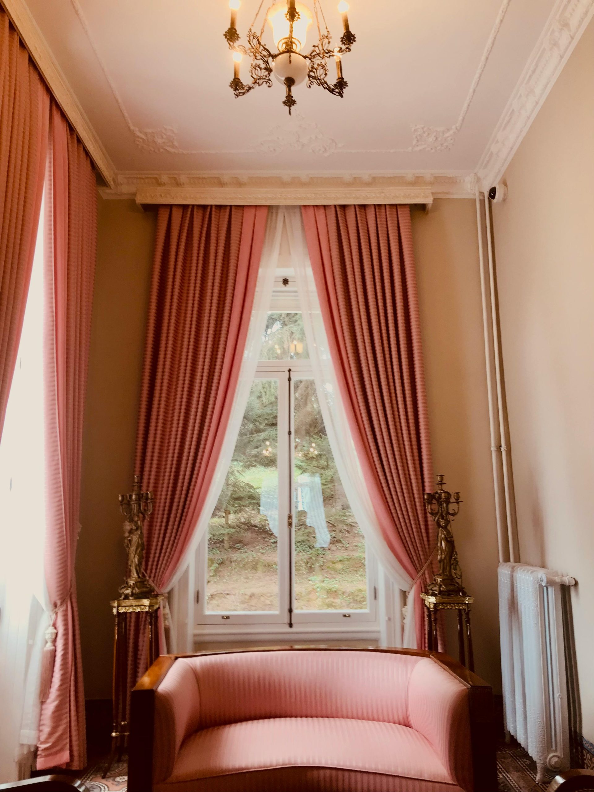 A luxurious vintage interior featuring elegant pink curtains, chandelier, and classic sofa.