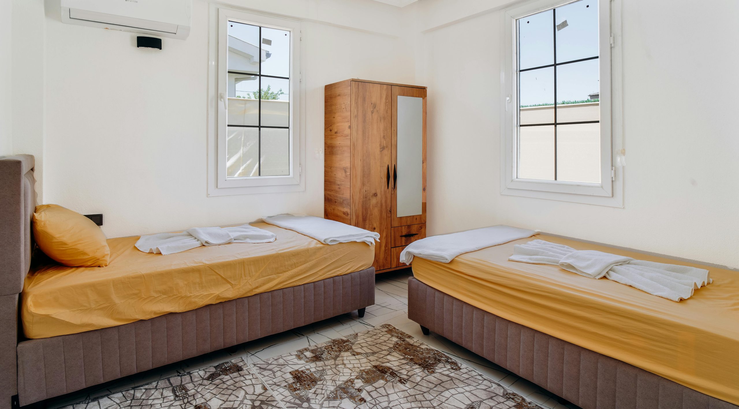 A minimalist bedroom featuring two neatly made twin beds with yellow sheets.