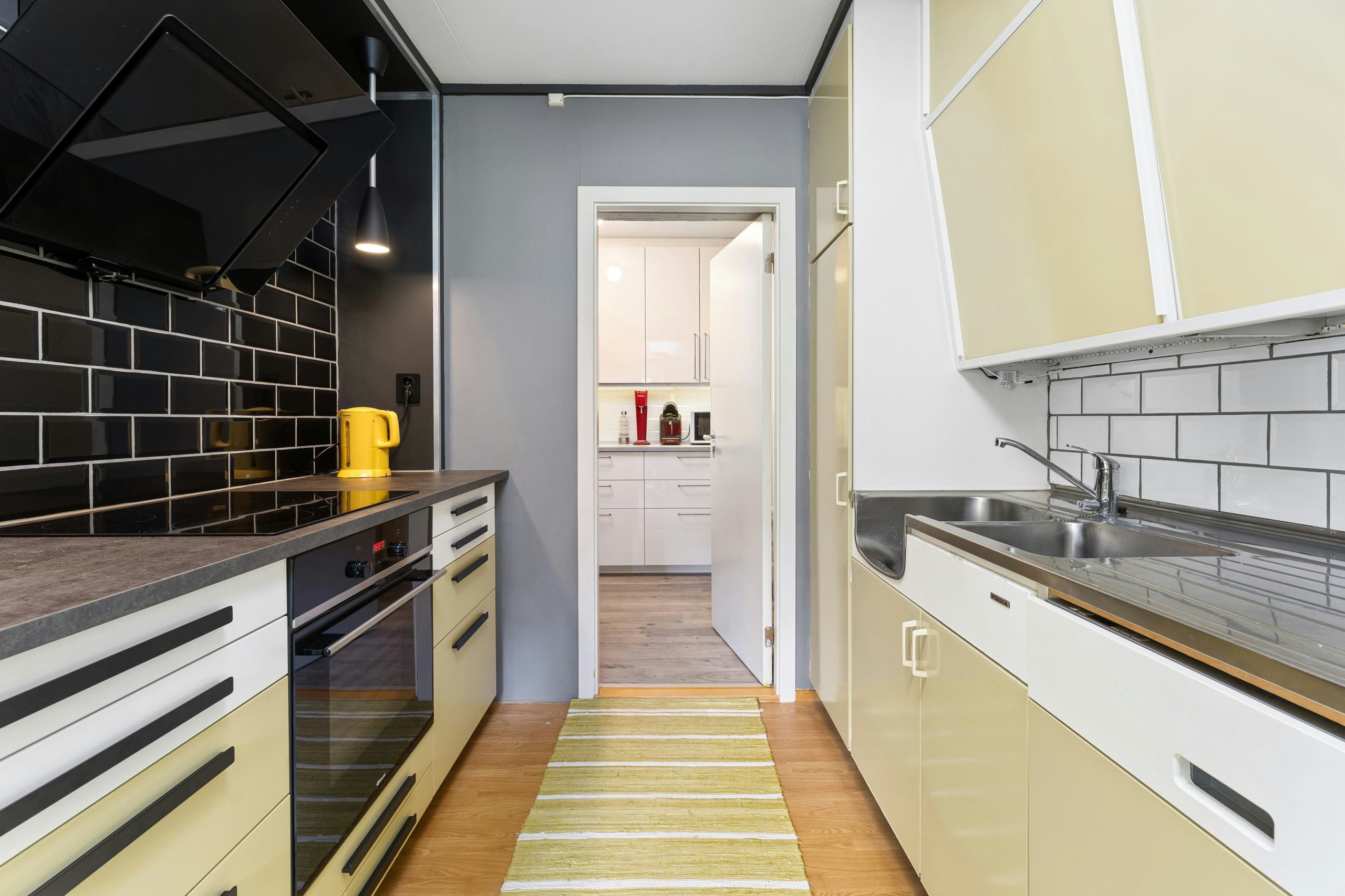A narrow kitchen with white and yellow cabinets