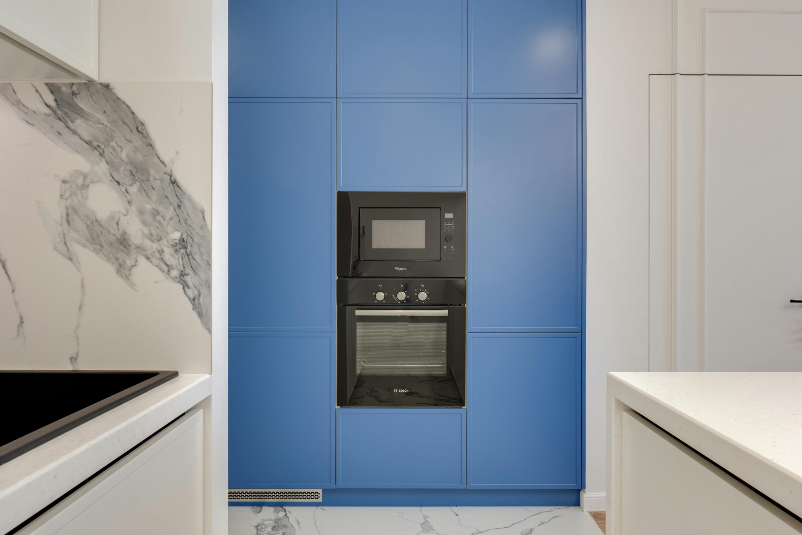 A sleek modern kitchen featuring blue cabinetry with built-in oven and microwave.