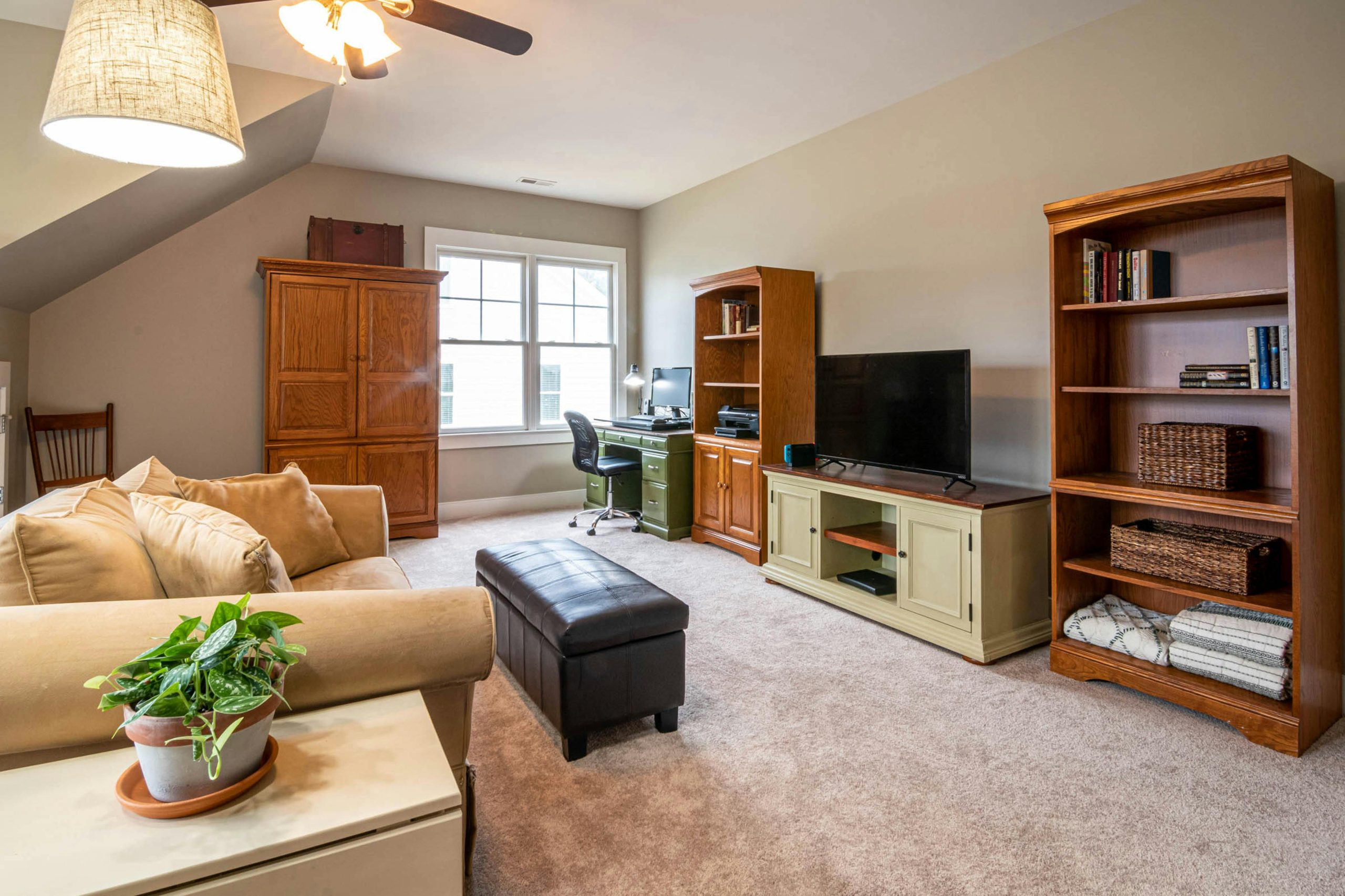 A well-furnished living room with a couch, television, and natural light from the window.