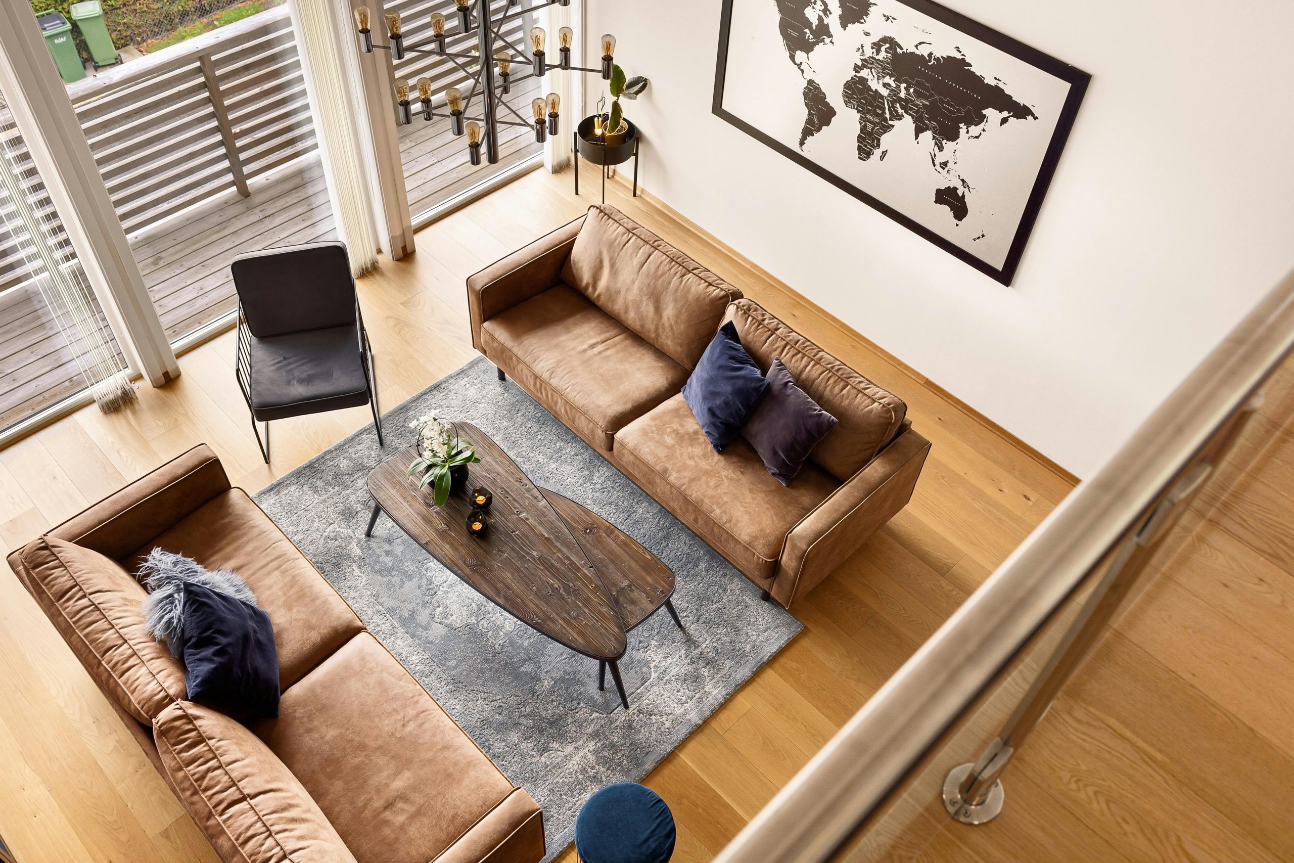 Aerial view of a modern living room with brown sofas, wooden floor, and world map decor.
