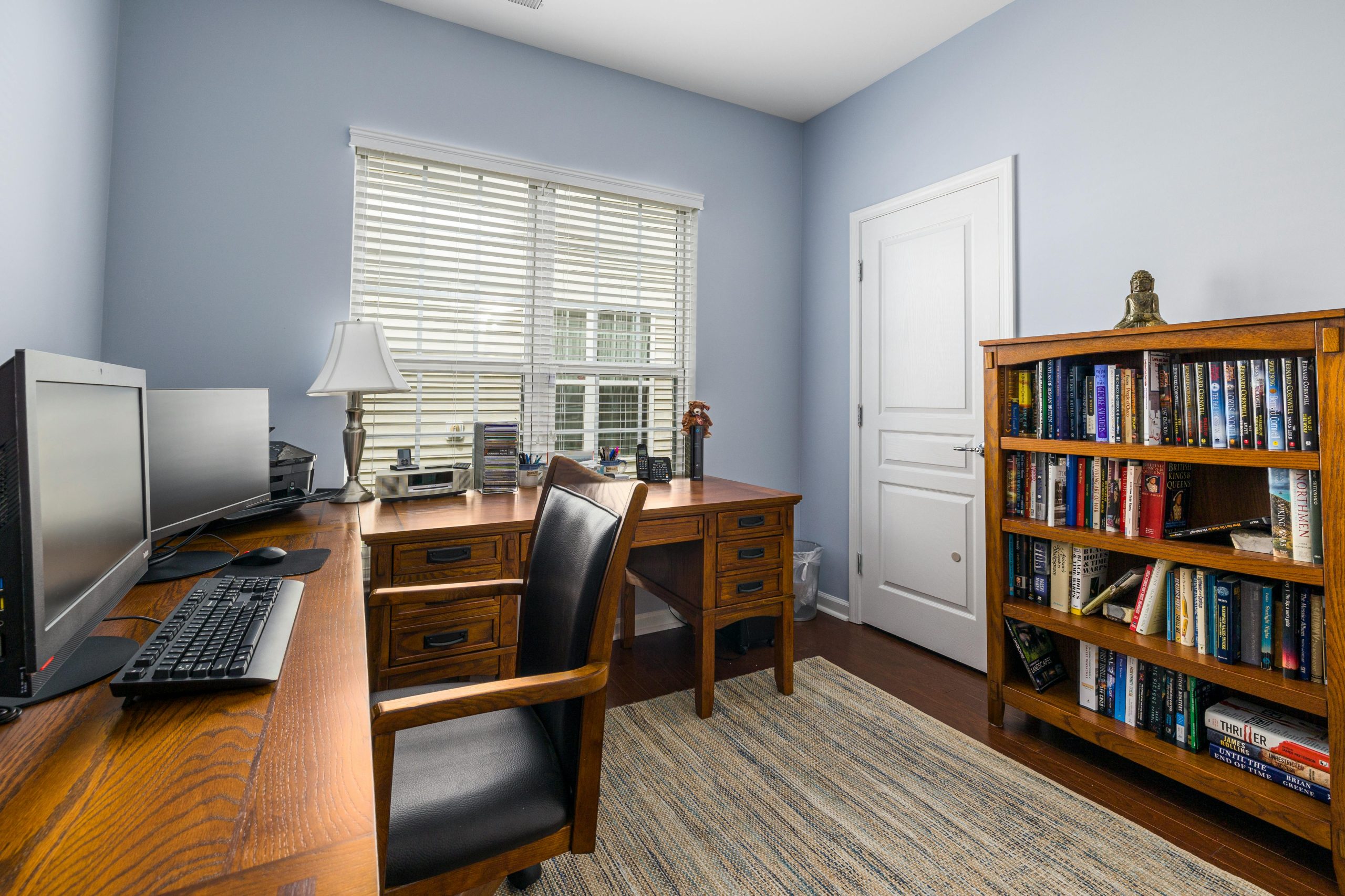 Bright home office featuring wooden desk, chair, computer setup, and bookshelves.
