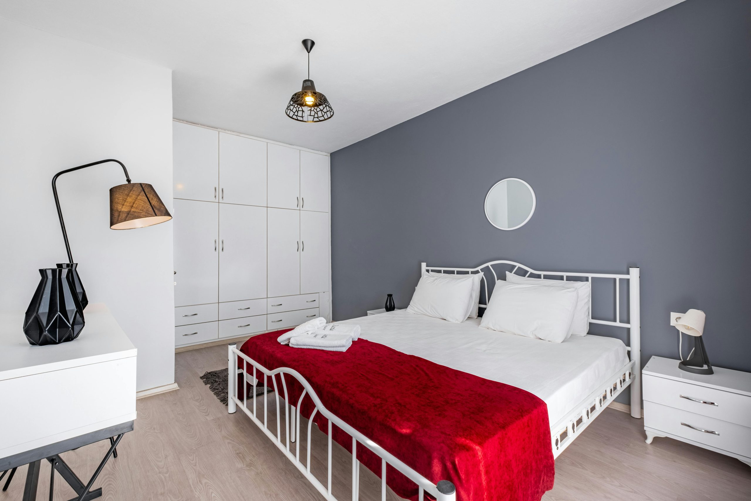 Contemporary bedroom featuring a white bed with a vibrant red blanket and minimal decor.