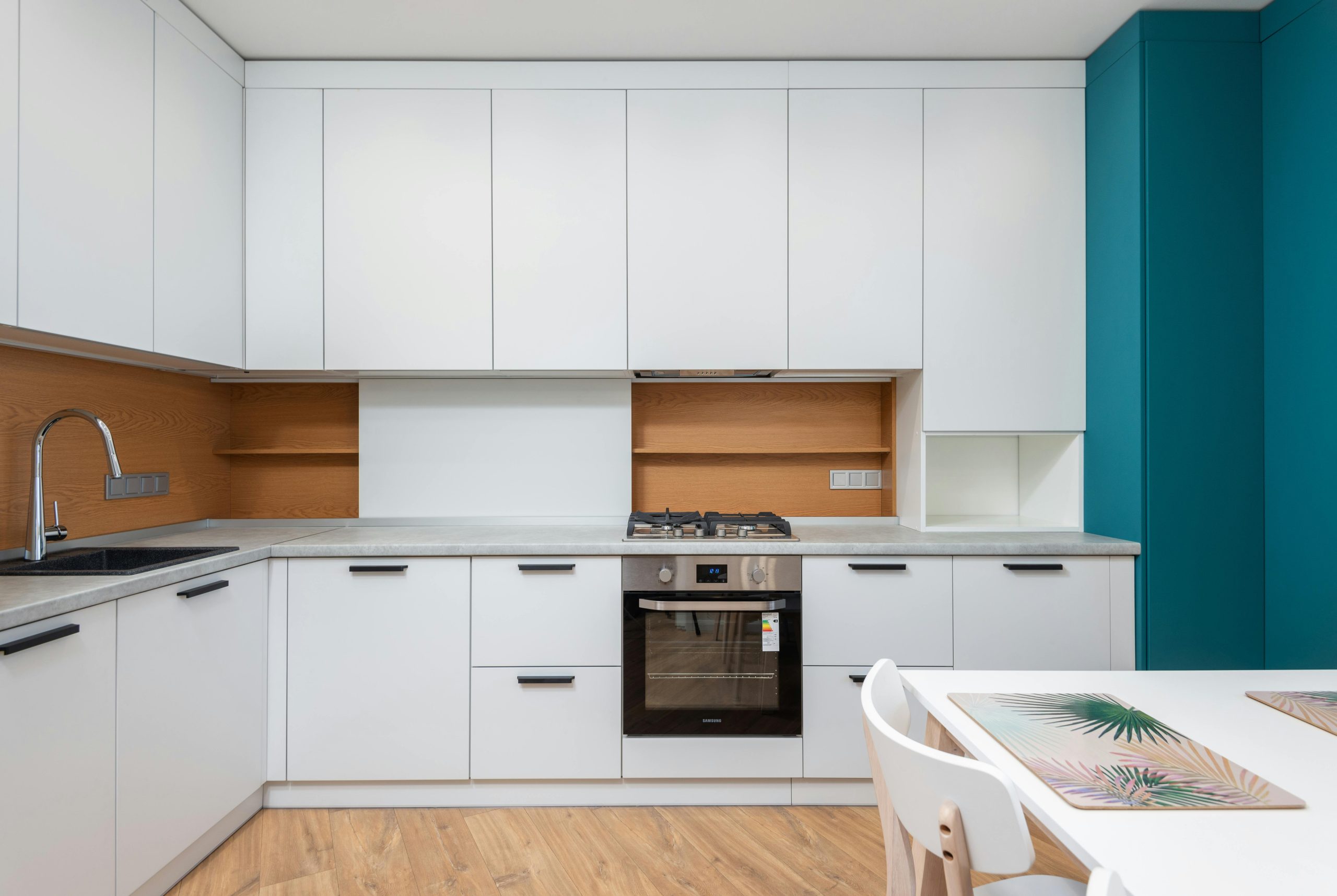 Contemporary kitchen interior with cabinets and gas stove above oven against table with placemats in house