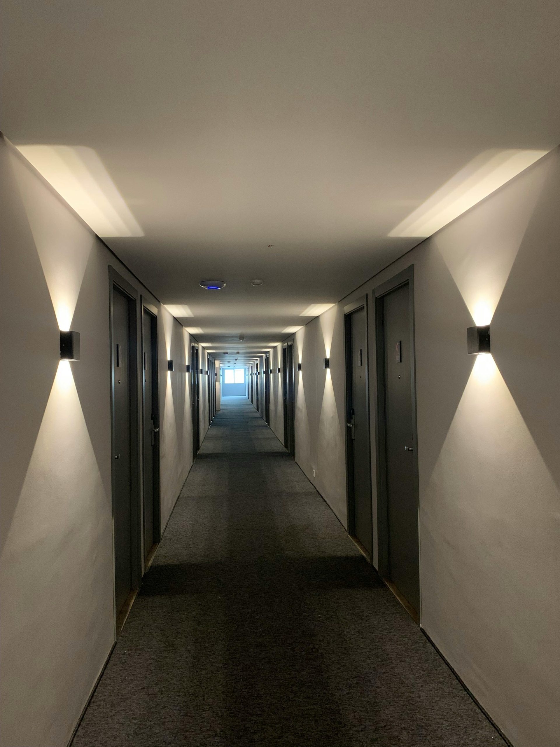 Dimly lit hotel corridor with symmetrical modern lights on white walls.