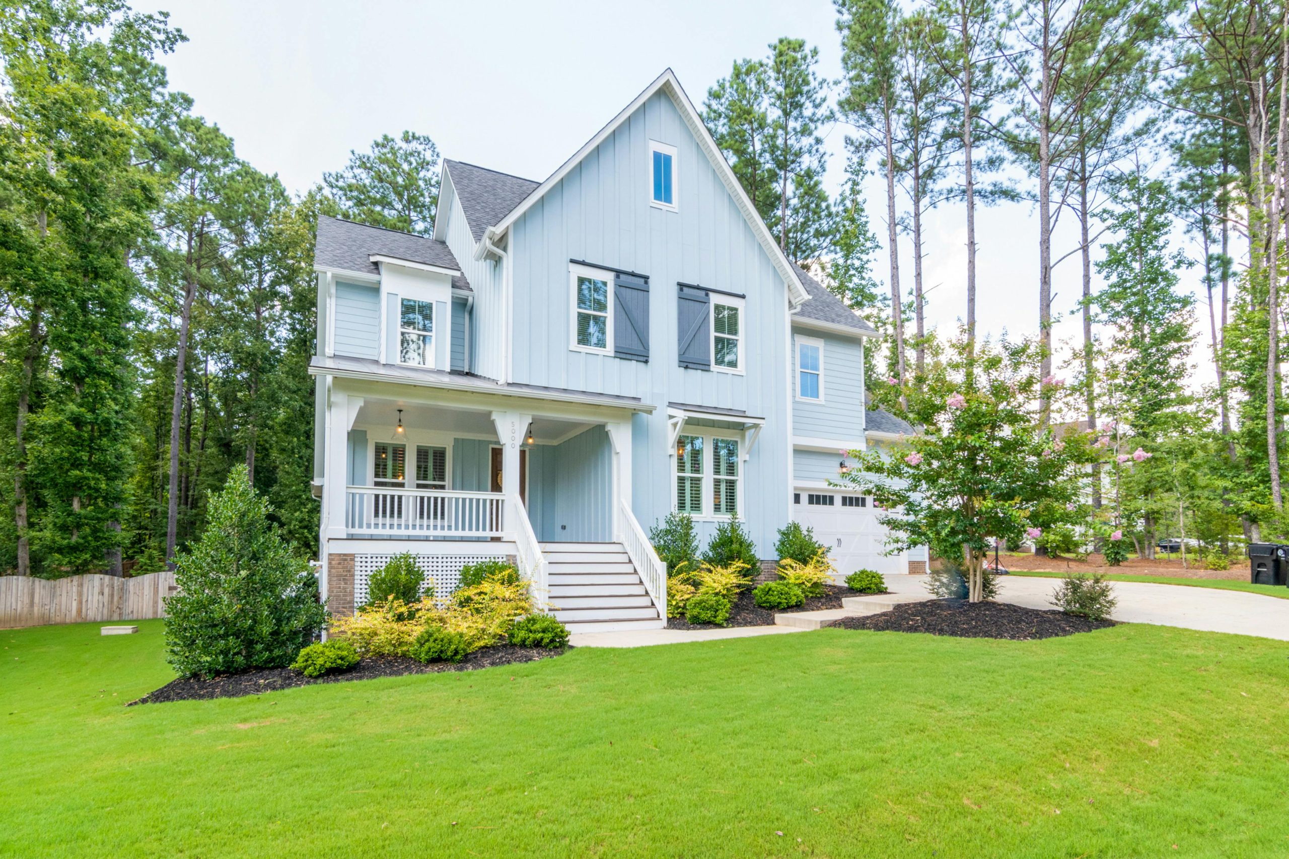 Elegant light blue suburban home with a lush lawn and forest backdrop.