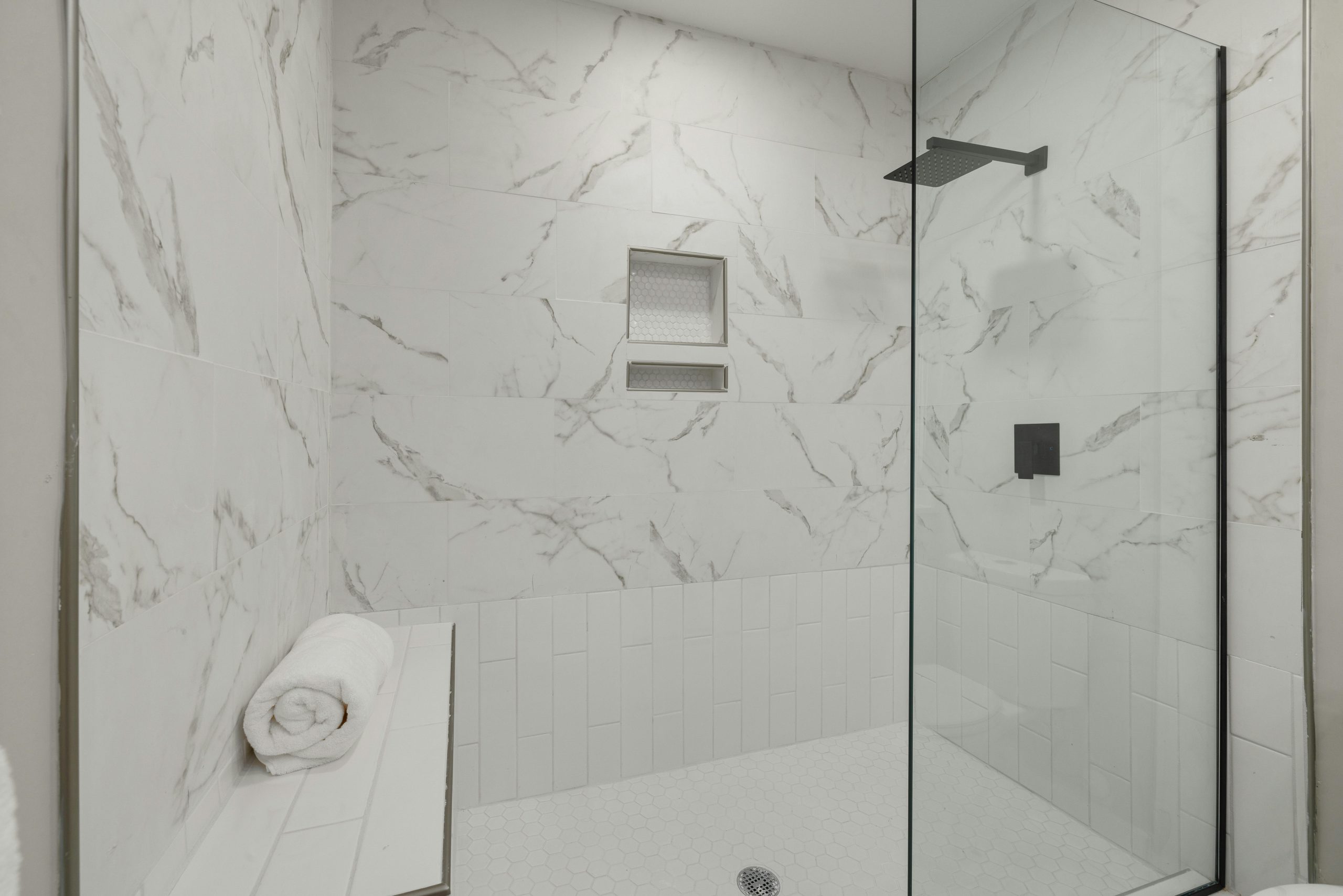 Elegant white marble shower with glass door, bench, and towel in modern bathroom.