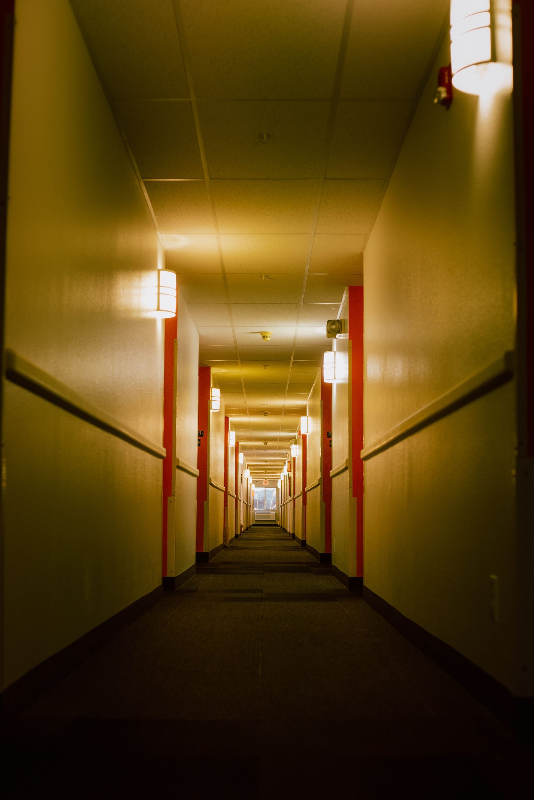 Explore the moody ambiance of a narrow hotel corridor with dim lights and geometric symmetry.
