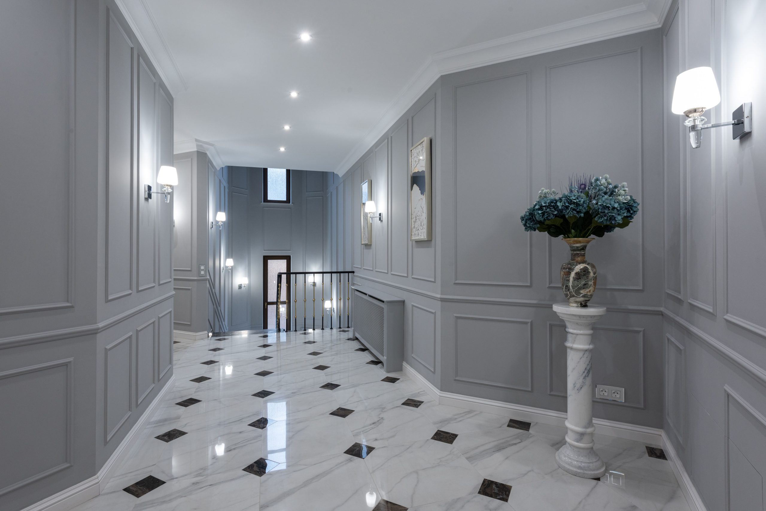 Gray walls and shiny marble floor in hallway of spacious classic styled villa decorated with paintings and lamps
