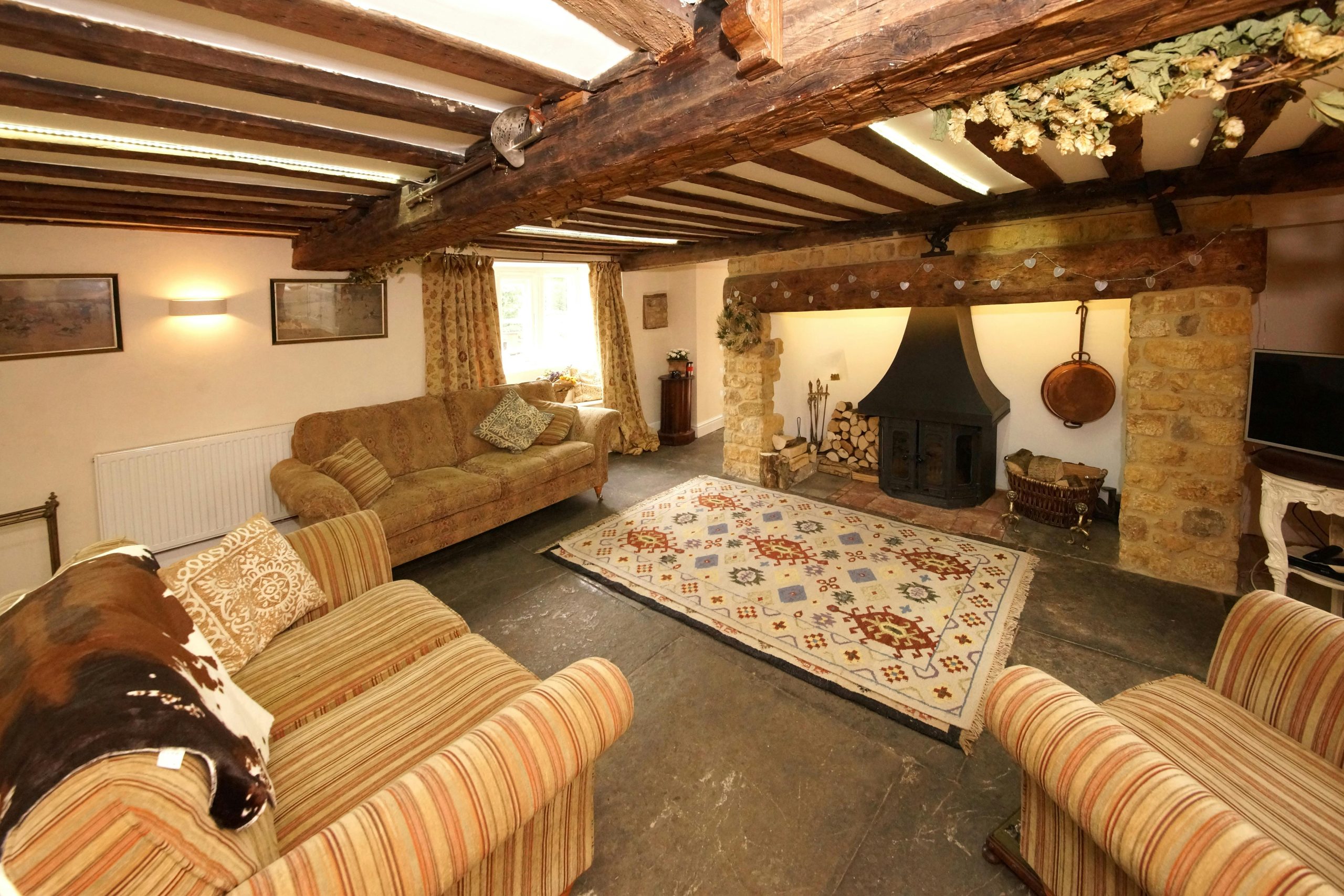 Inviting living room with rustic decor features exposed beams, patterned rug, and a traditional fireplace.