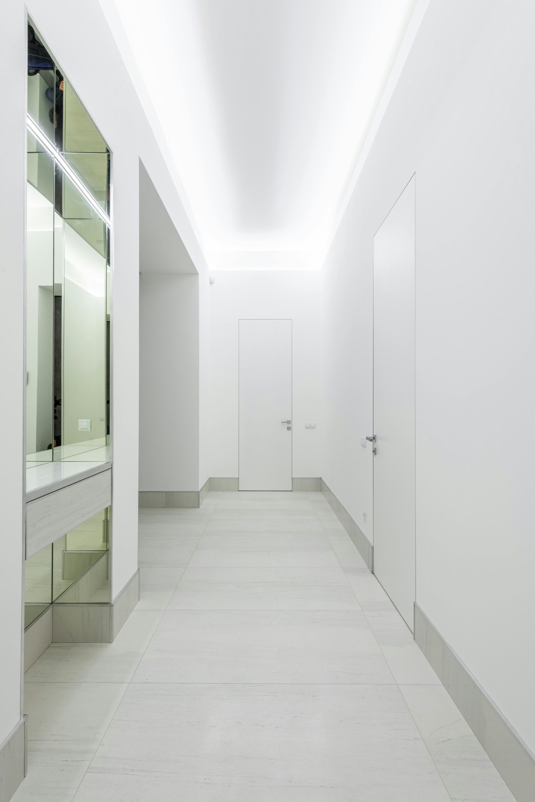 Long narrow brightly lit corridor with glass reflective surface and white doors at home with stylish design and glowing lights