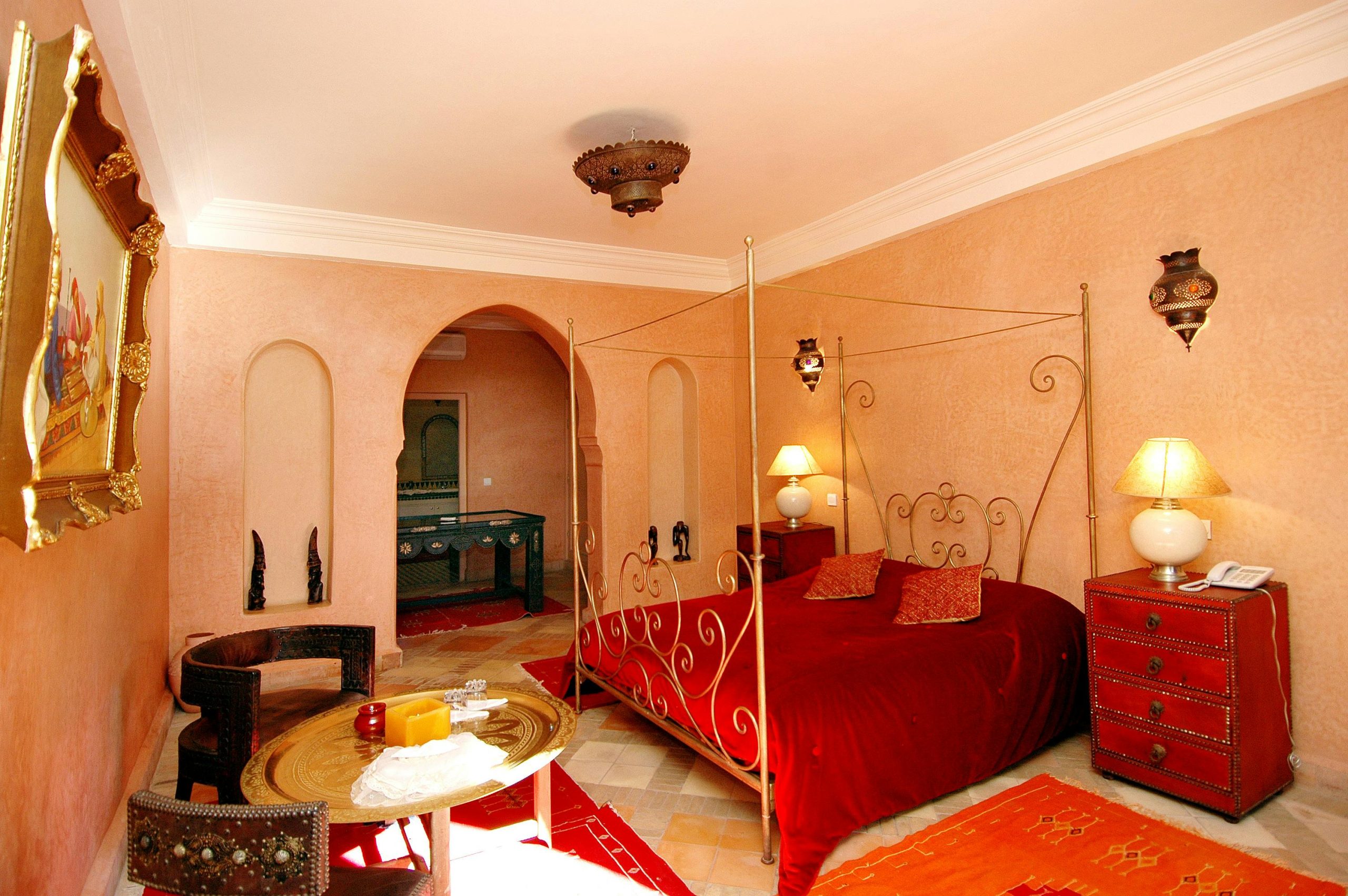 Luxurious Moroccan-themed bedroom featuring a red canopy bed, ornate decor, and warm lighting.