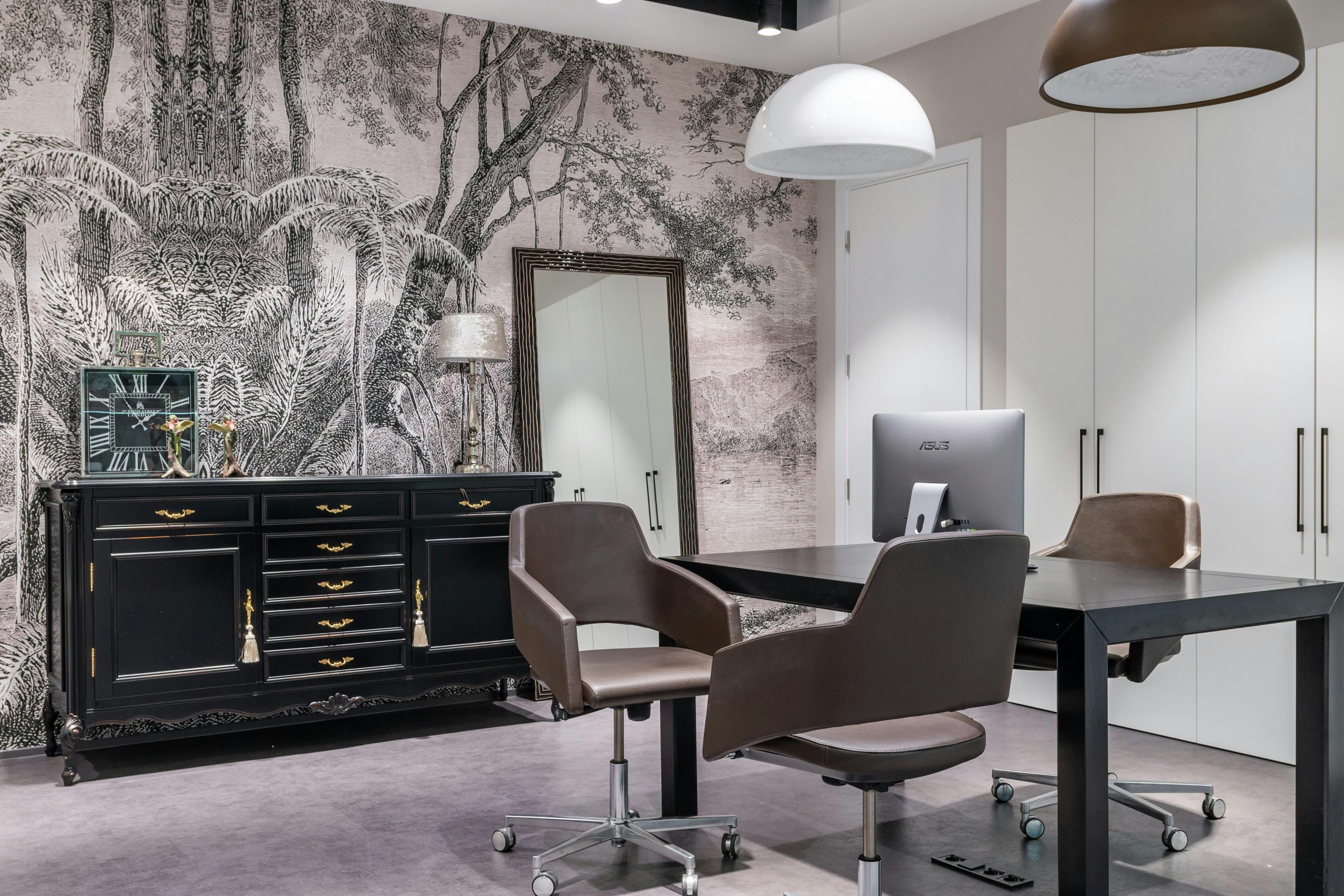 Modern computer on black table near armchairs placed in living room near cabinet with clock in spacious apartment with mirror and closet