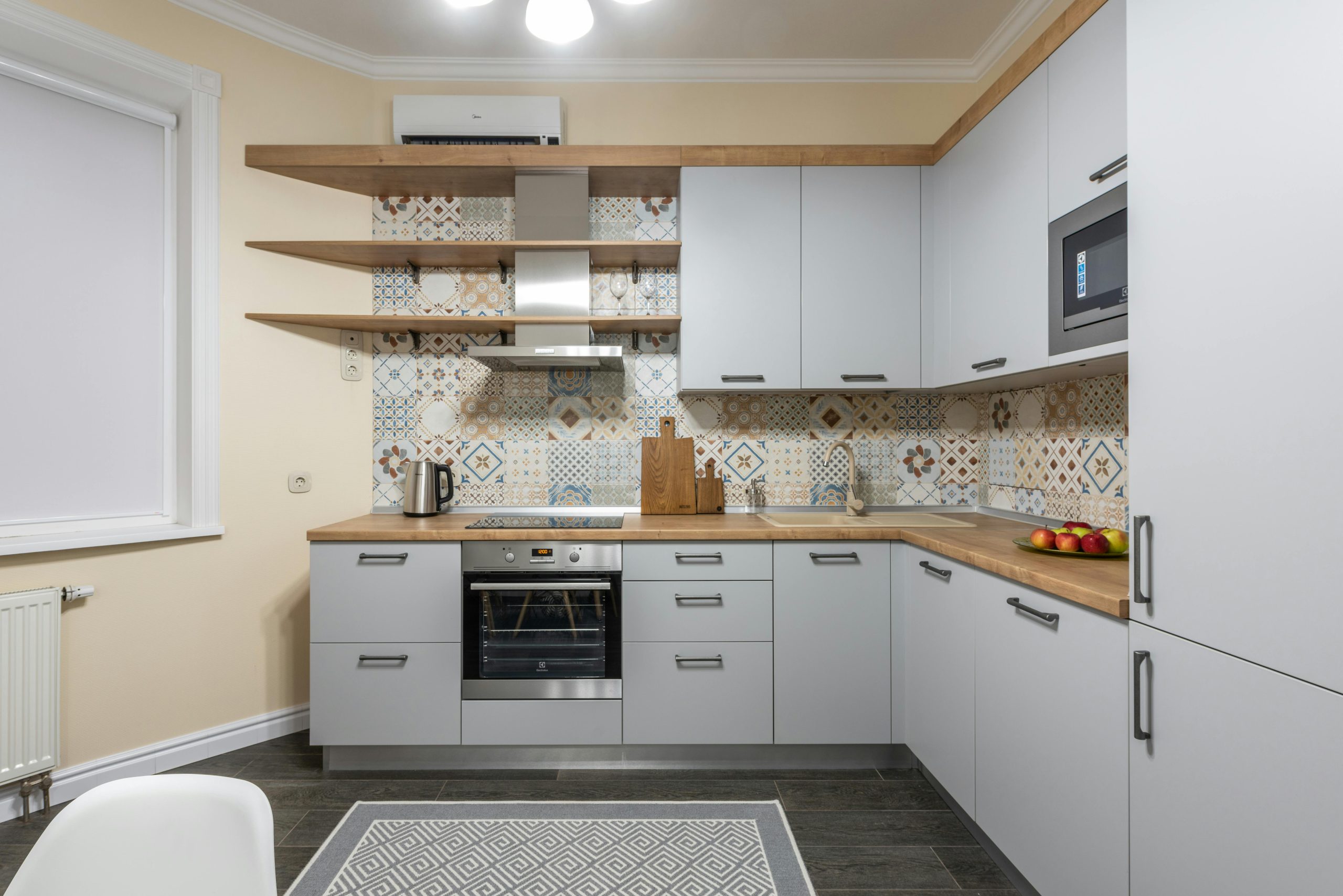 Modern kitchen with cabinets and electric stove with oven under hood illuminated by shiny lamp in house