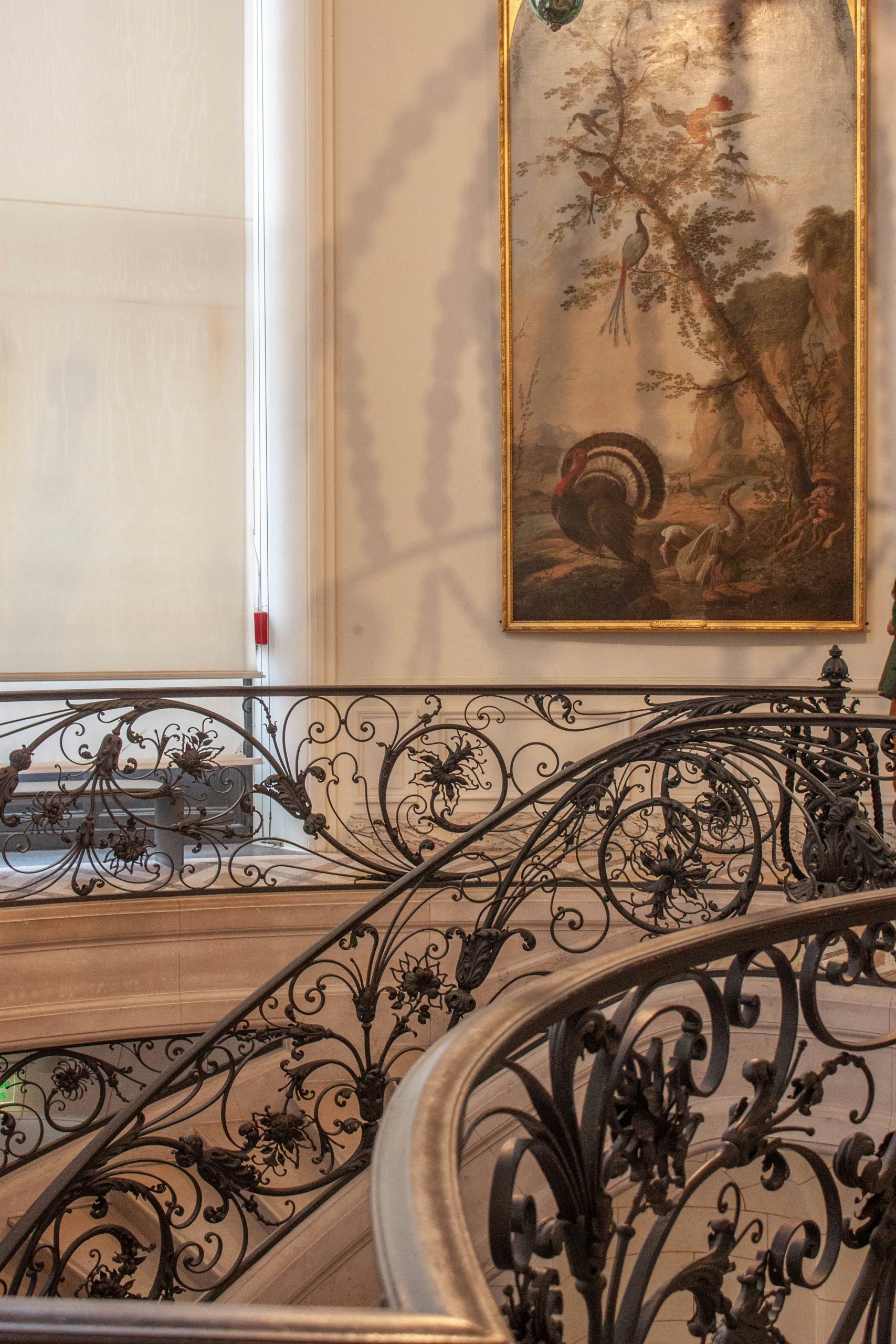 Ornate metal railing on a grand staircase with painting.