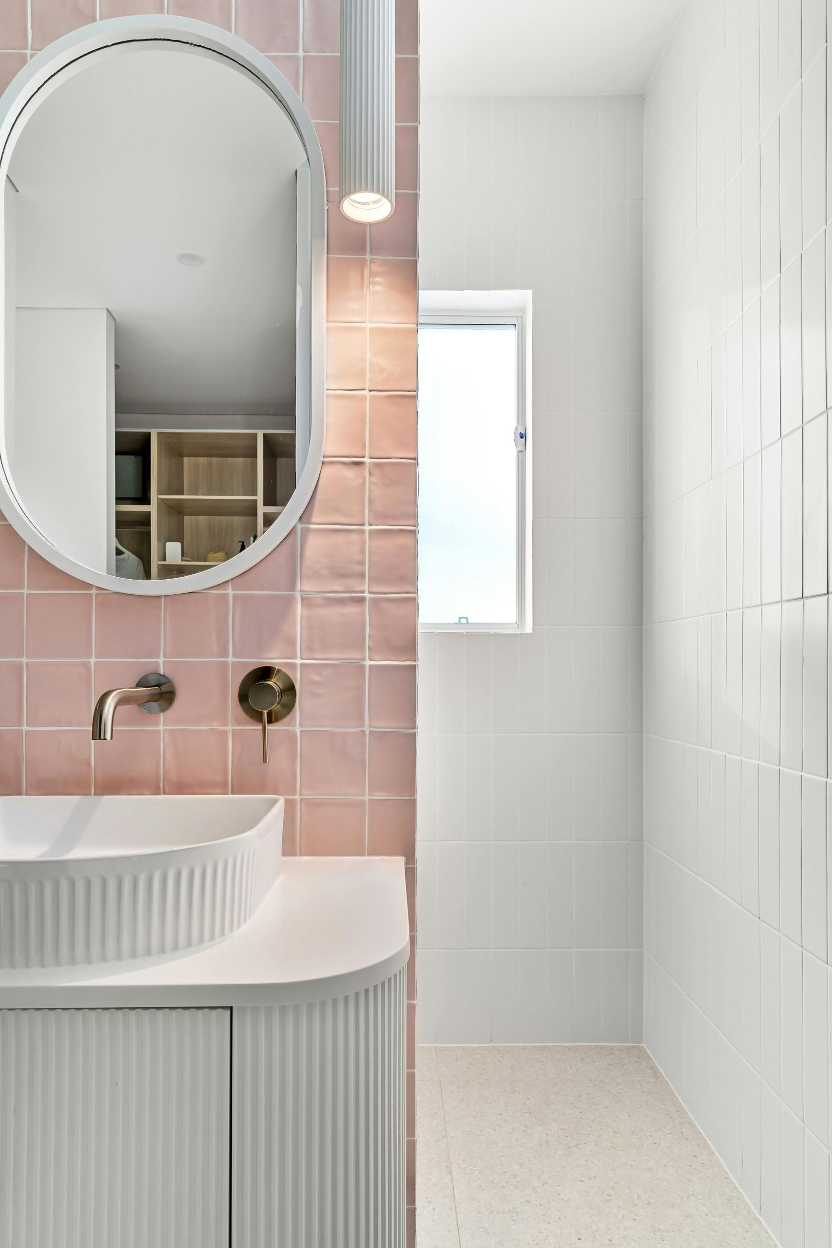 Stylish contemporary bathroom featuring a pink tile wall, oval mirror, and modern sink.