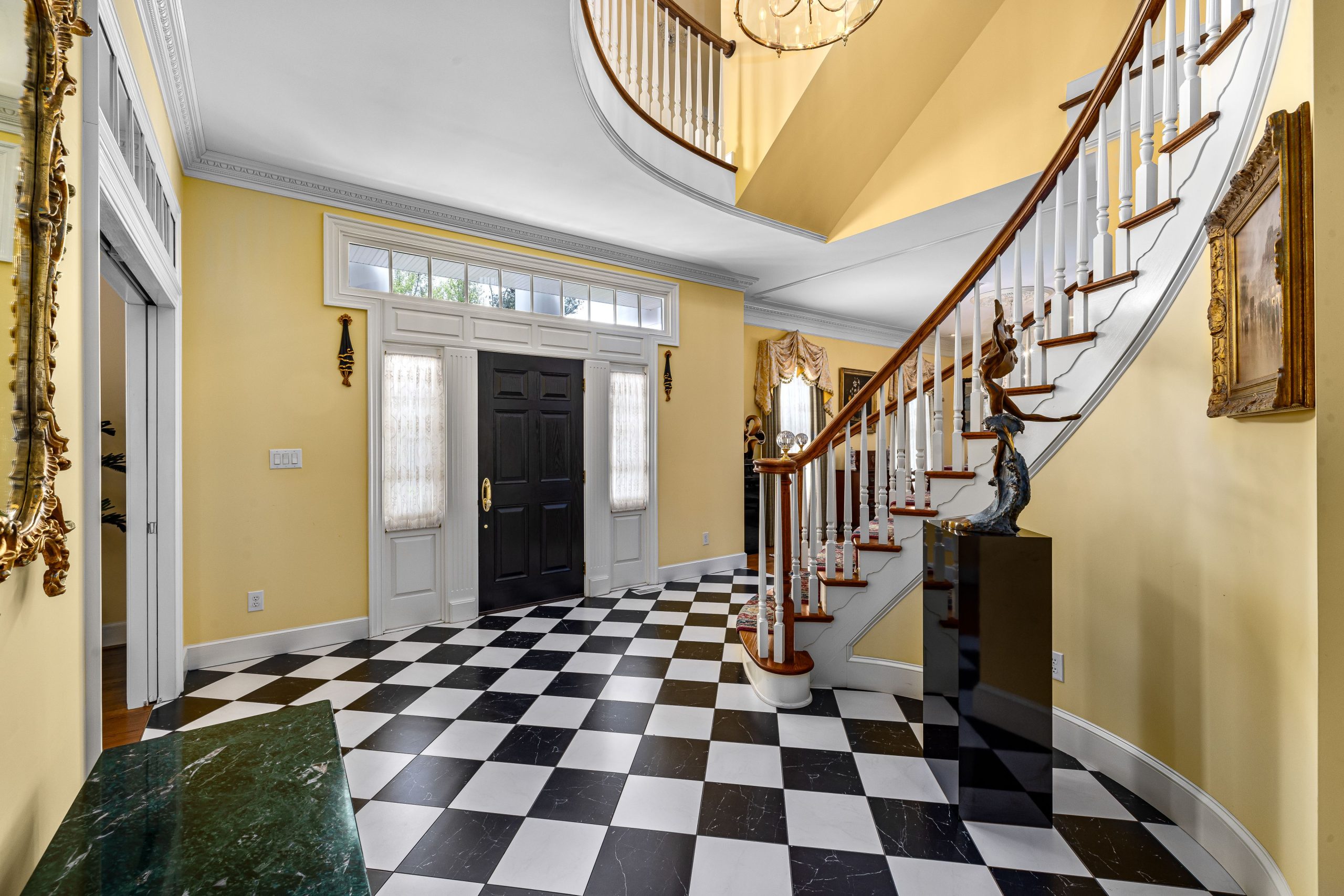 A luxurious mansion entryway with a black and white checkered floor and curved staircase.