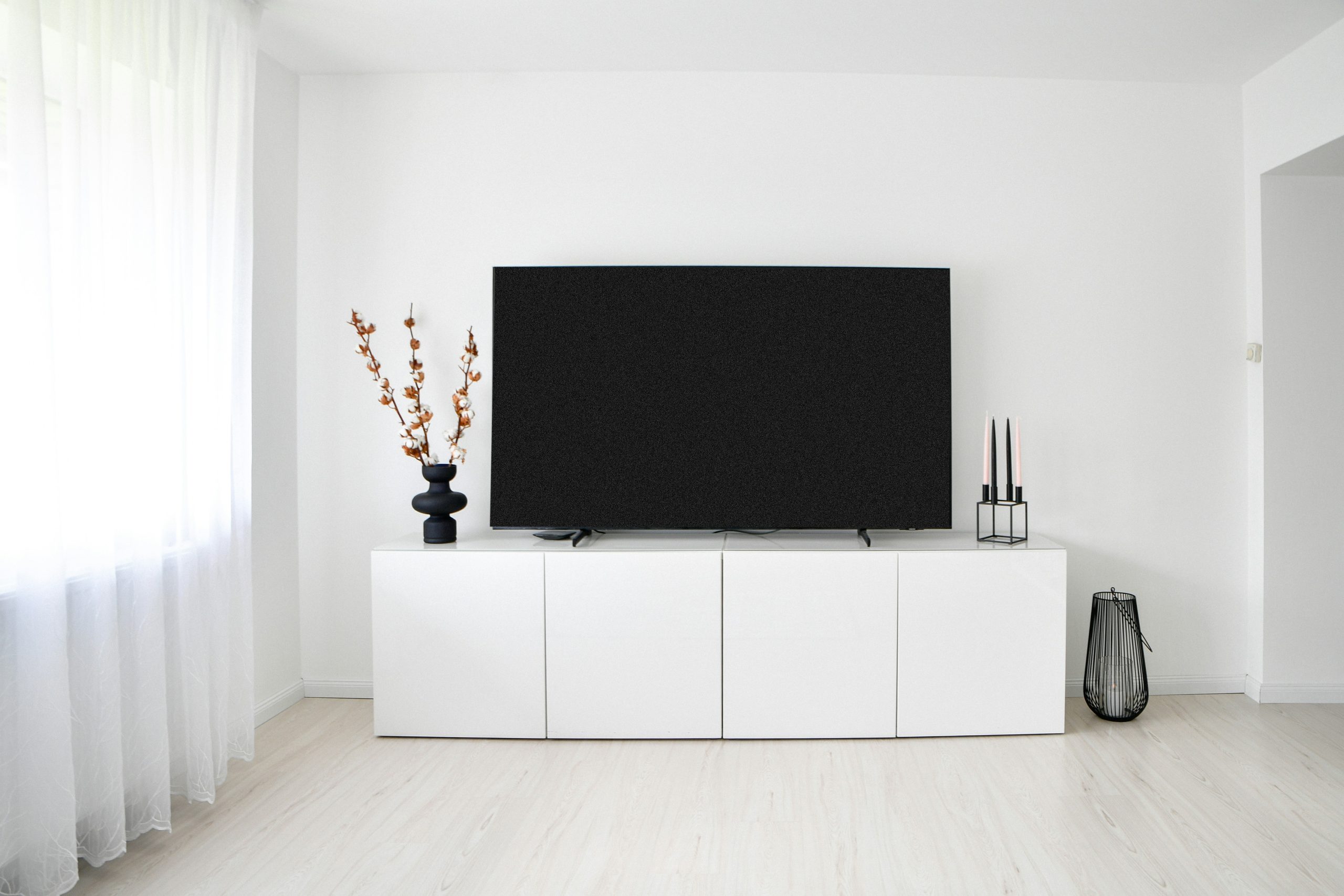 A modern minimalist living room interior featuring a large flat-screen television on a sleek white media console cabinet against a clean white wall.📸 Photo by me IG: @margoevardson