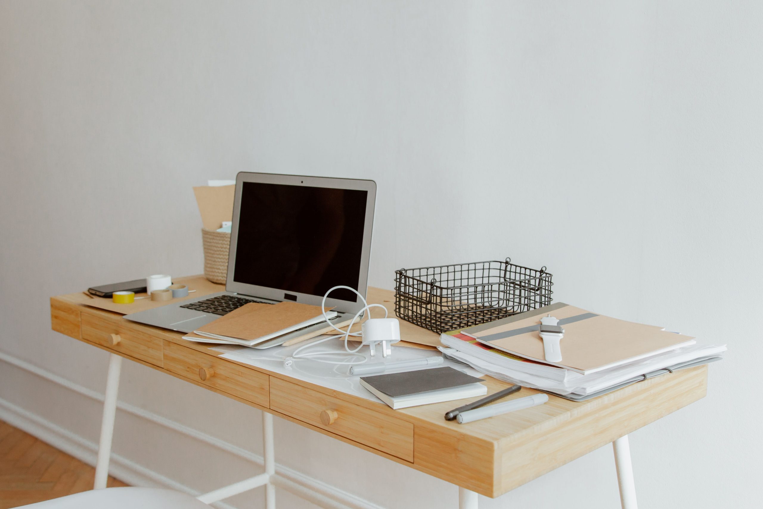A neatly organized desk with a laptop, notebooks, and office supplies in a minimalist office setting.
