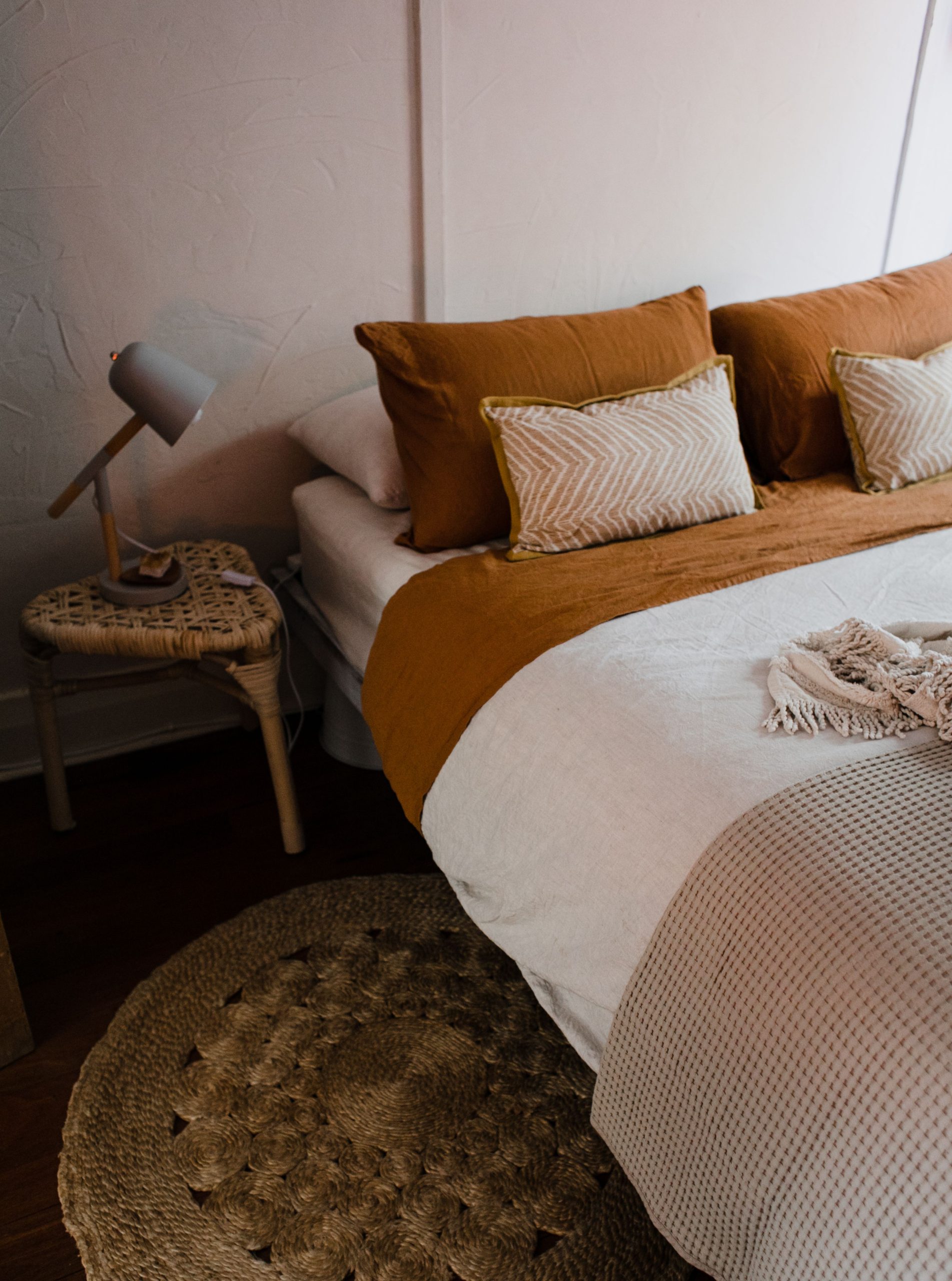 A stylish and cozy bedroom featuring earthy tones with a woven rug and bedside lamp.