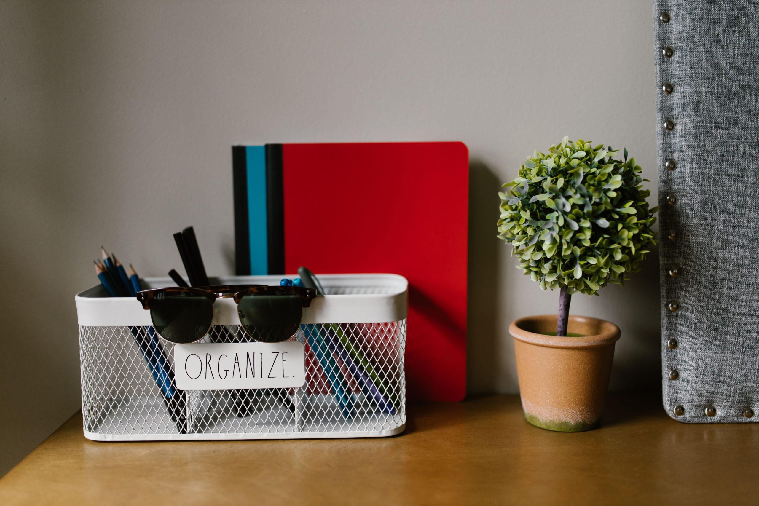 A tidy workspace featuring a basket with stationery, a mini tree, and a colorful notebook.