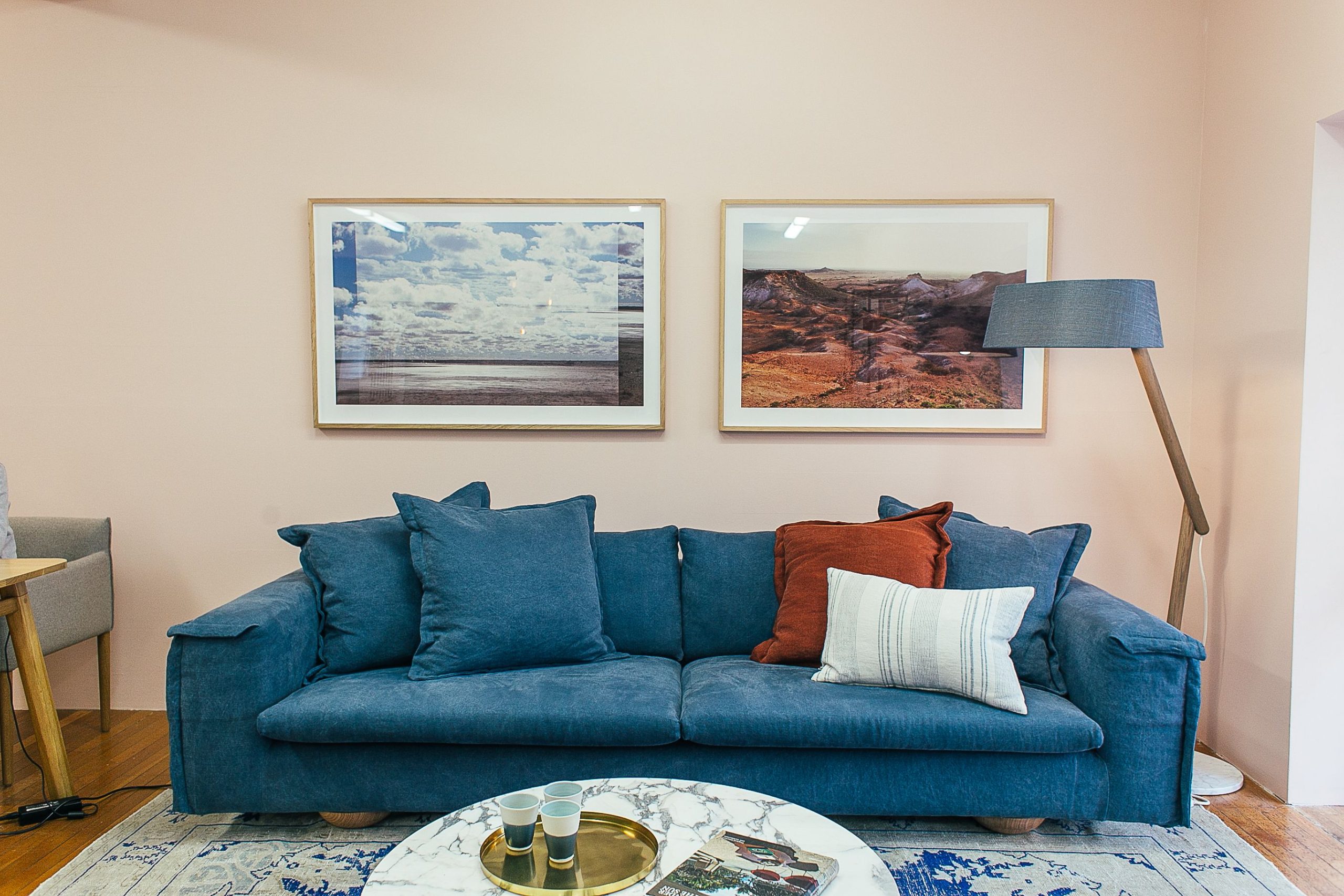 Big comfortable blue sofa with soft cushions placed in modern living room with round marble table near wall decorated with framed pictures