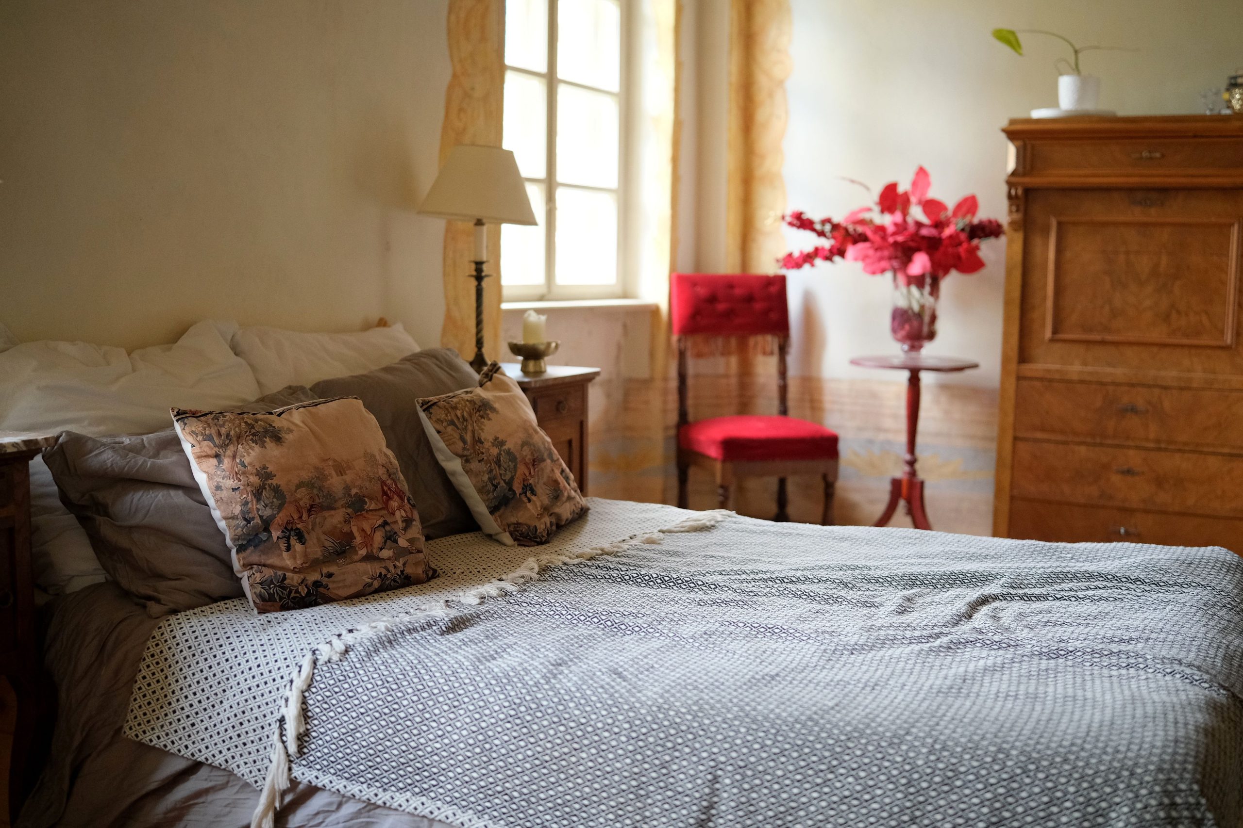Charming vintage-styled bedroom featuring a cozy bed with decorative cushions and vibrant floral arrangements.