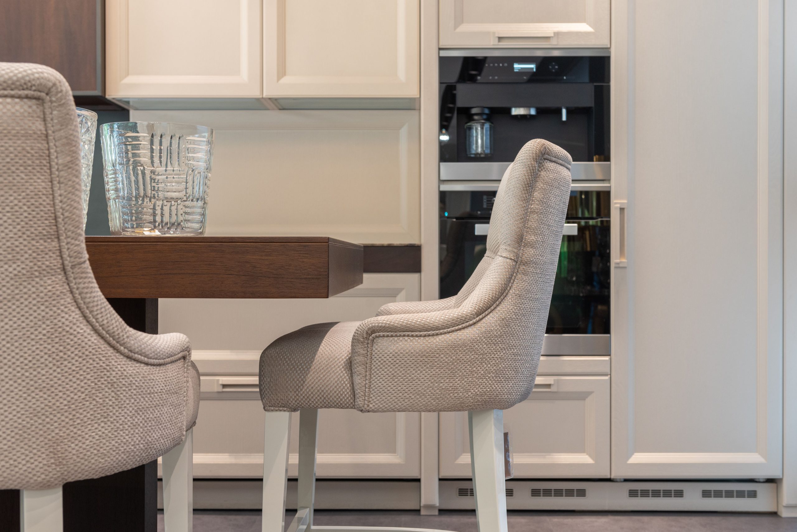 Comfortable armchairs and wooden table with glassware against simple white kitchen cabinets in light spacious kitchen