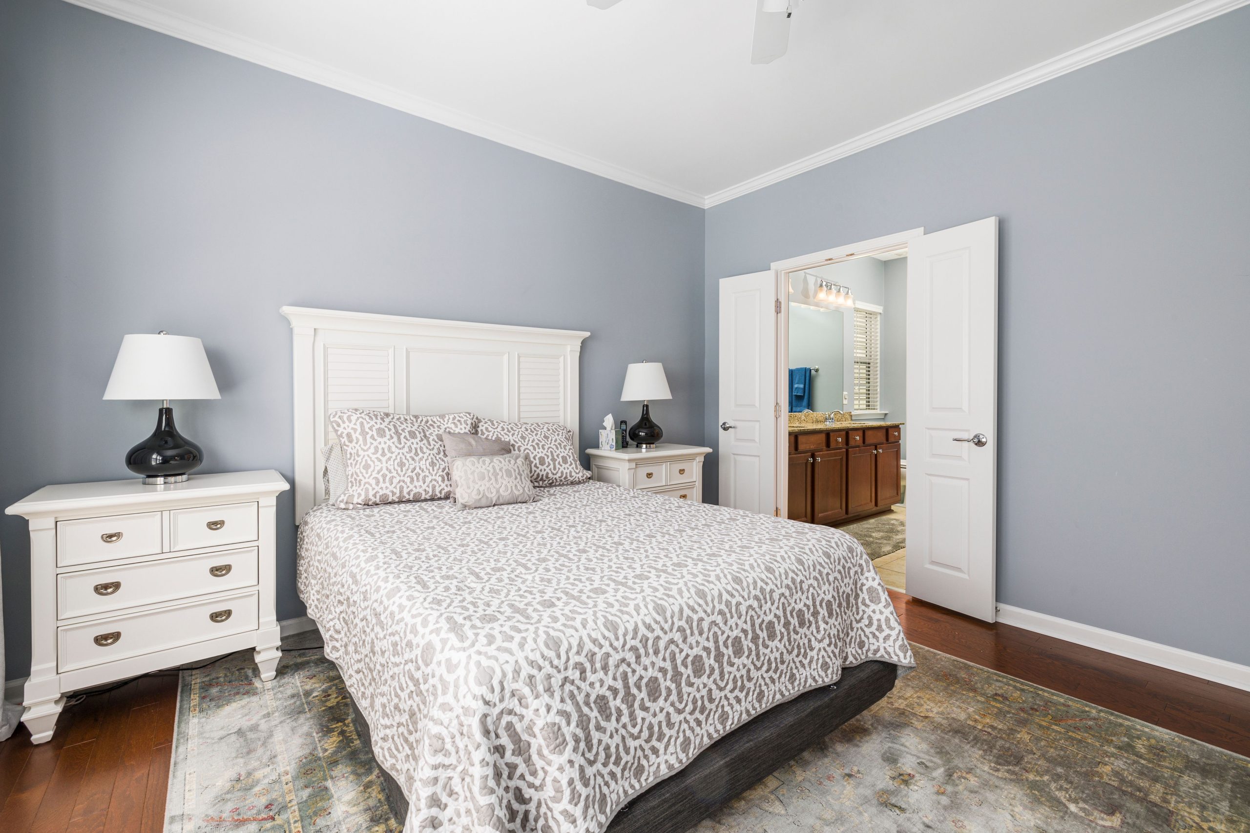 Elegant bedroom with patterned bedding, white furniture, and a view into the bathroom.