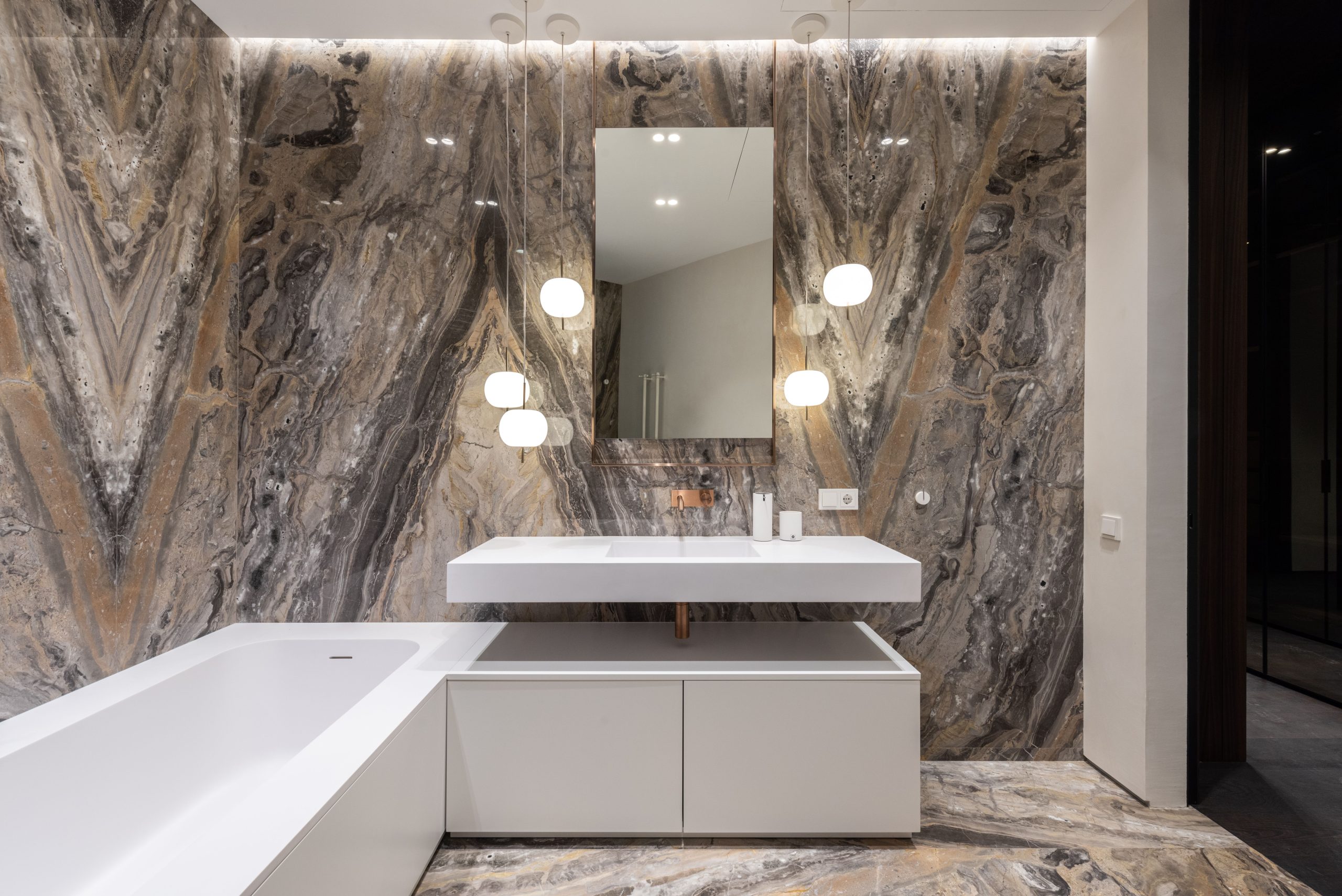 Interior design of modern bathroom with mirror hanging on wall above sink and big bathroom and illuminated with round lamps
