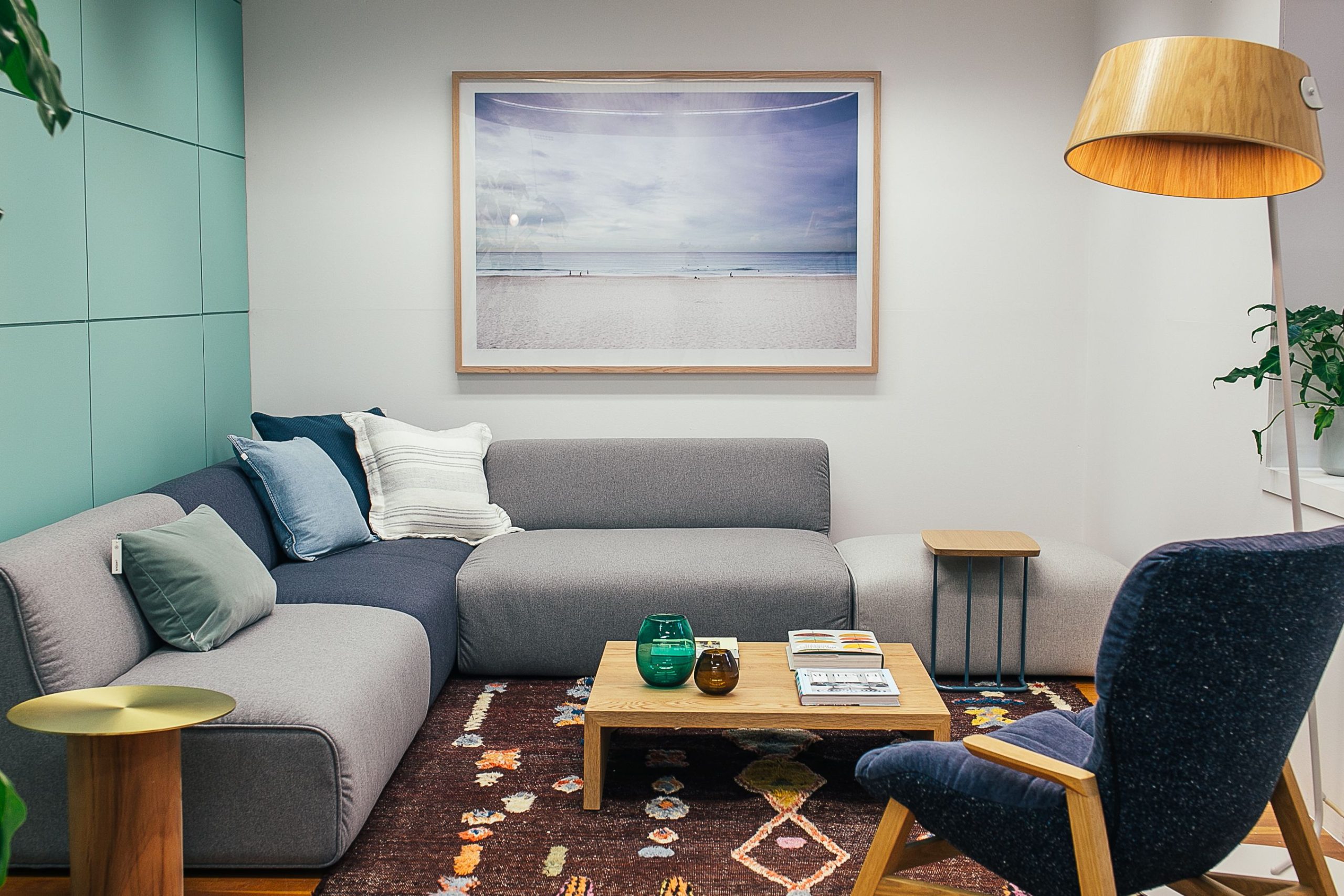 Soft gray sofa with cushions and wooden coffee table placed near armchair in living room with floor lamp and painting on wall