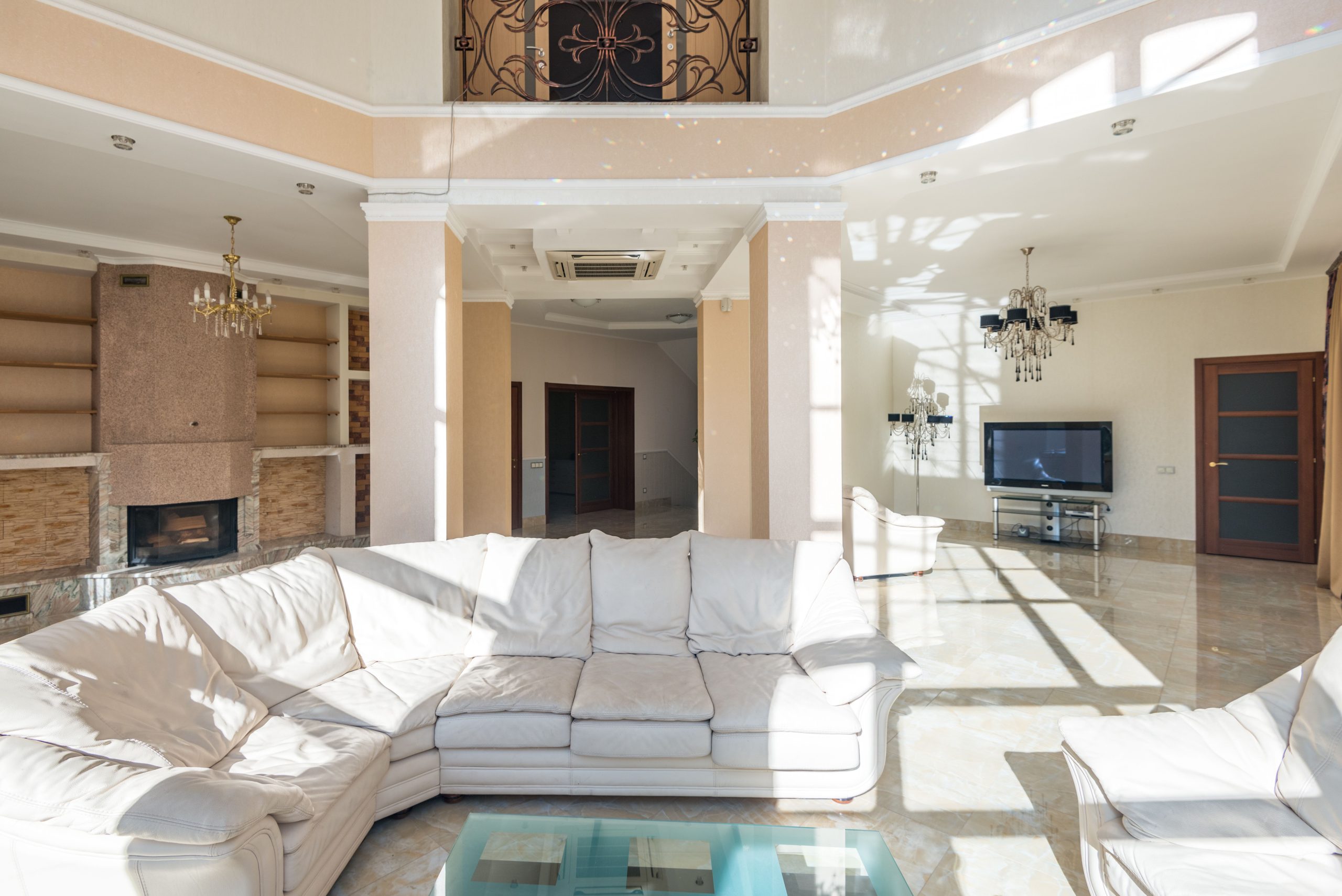 Spacious luxury living room with modern decor, sectional sofa, chandeliers, and TV.