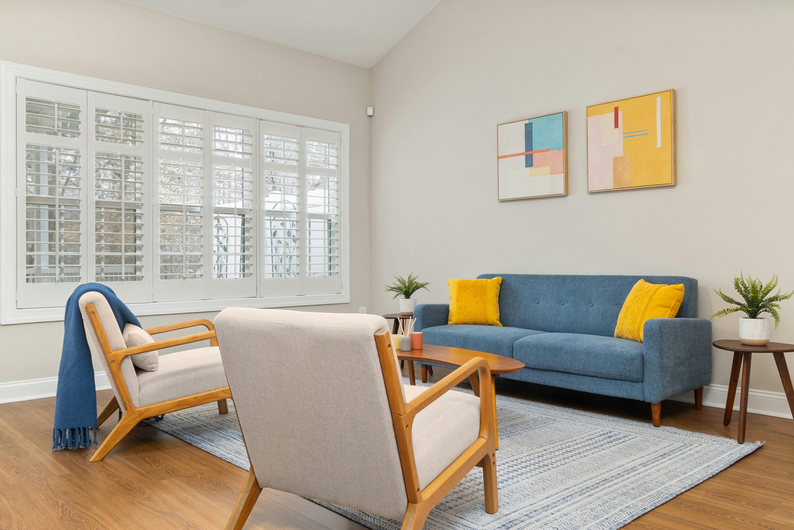 Stylishly designed living room featuring a blue sofa, abstract art, and natural light from large windows.
