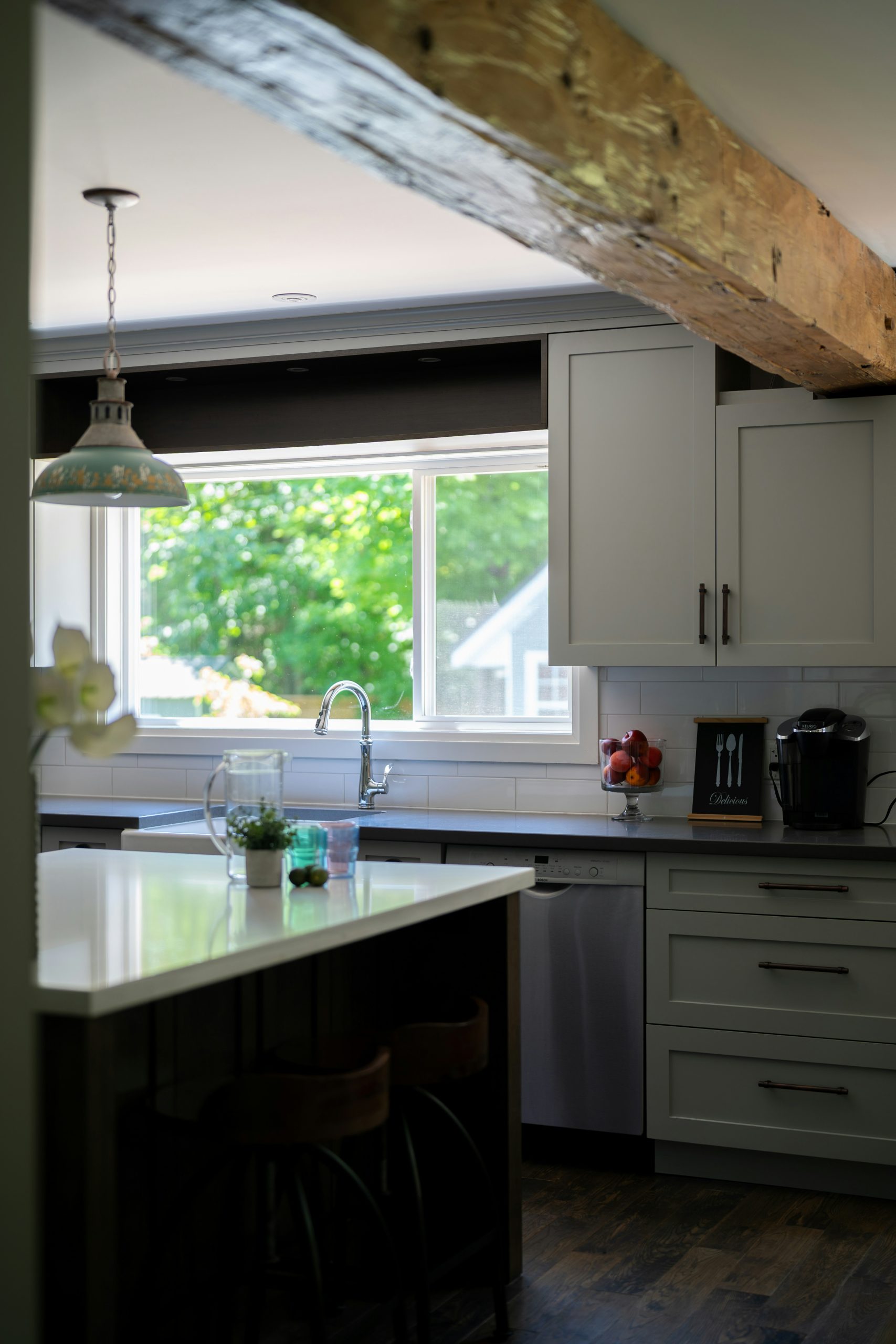 Bright kitchen interior with island, wooden beam, and green view.