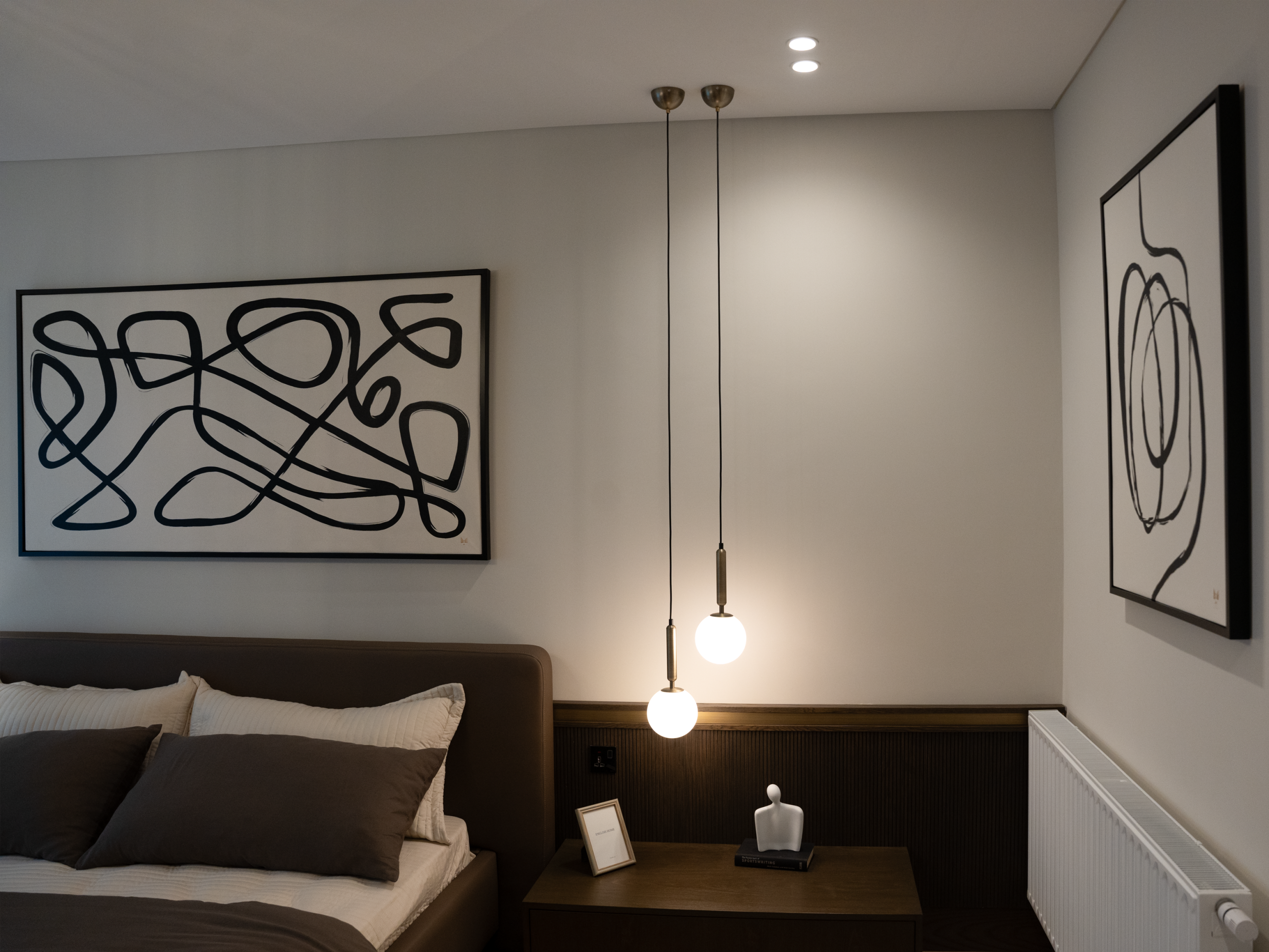 Elegant bedroom with modern art, pendant lights, and cozy bedding.