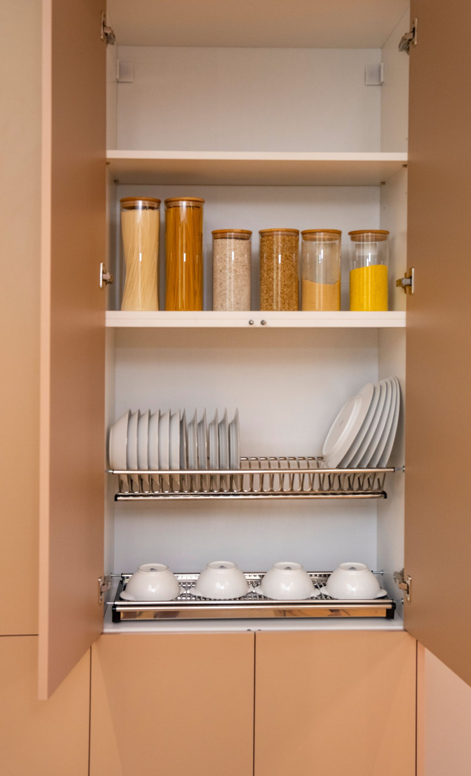 Neatly organized kitchen cupboard showcasing dishes and dry goods in jars.