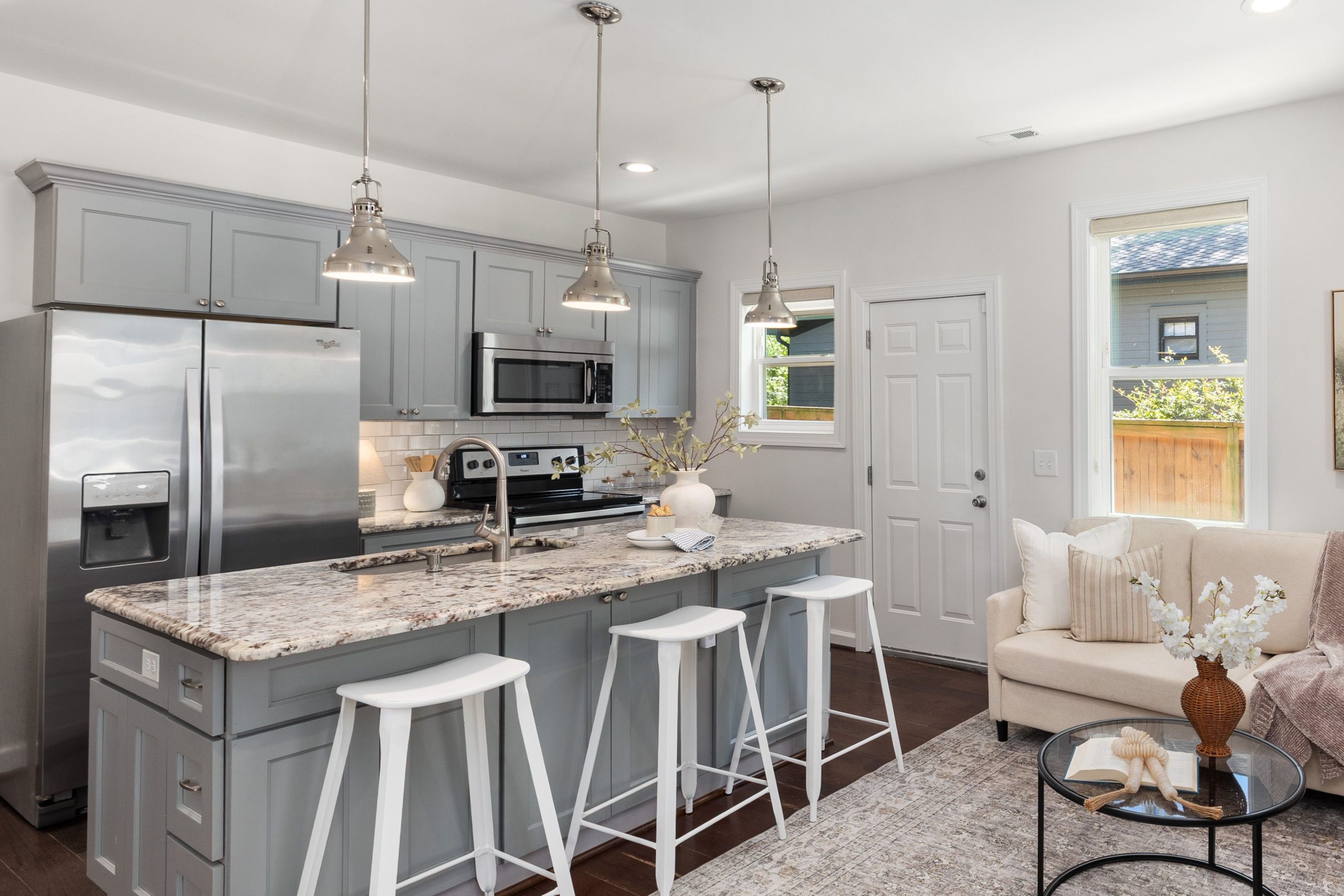 Stylish gray kitchen with granite island, pendant lights, and stainless steel appliances.